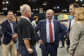 Greg Abel is pictured at the center of a group of people conversing in an indoor event space