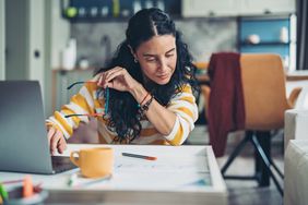 Woman sitting at her desk working on a laptop and studying some notes.