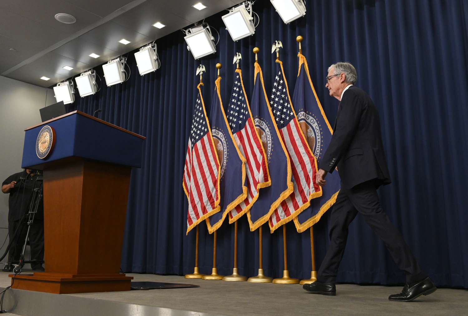 Jerome Powell walks across a stage, toward a podium. Behind him are U.S. and Federal Reserve flags.