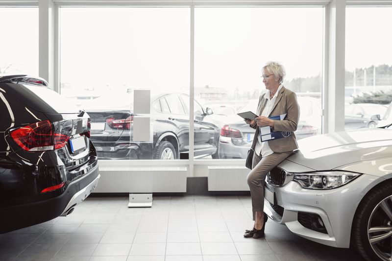 A woman leans on a car at a dealership.