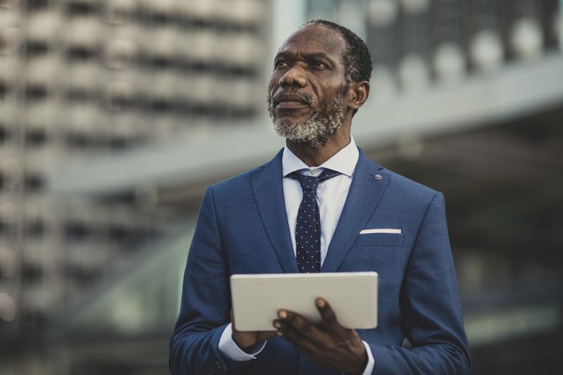 Businessman in a suit standing outside a building looks outward with a tablet in his hand