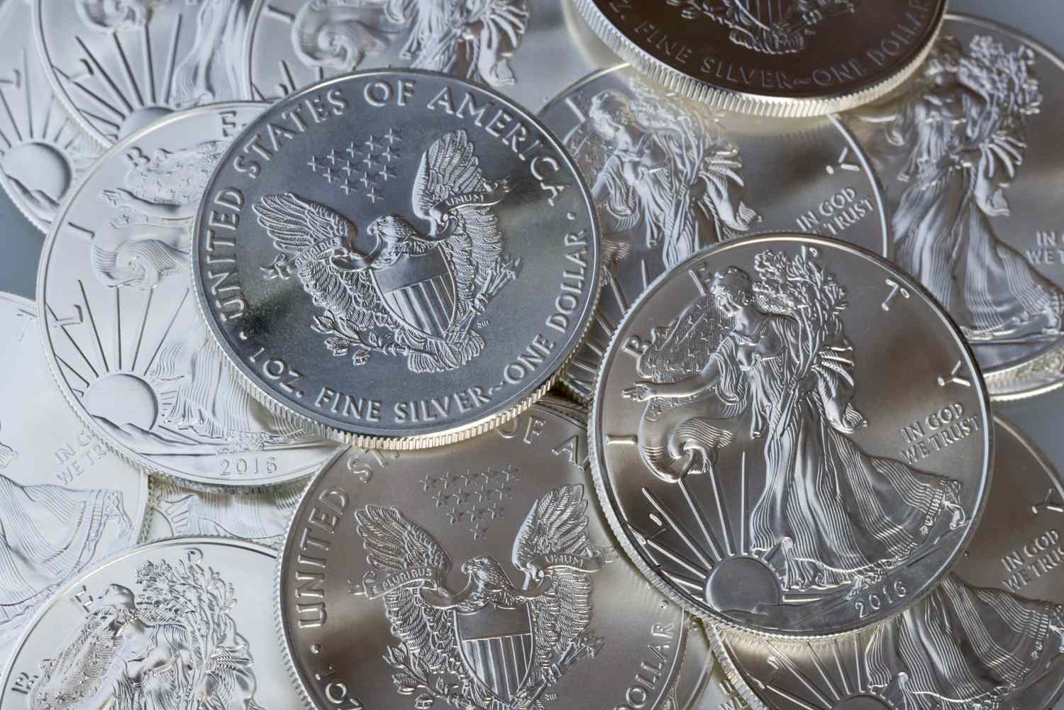 One dollar silver bullion coins lay in a layer showing heads and tails of the coins.
