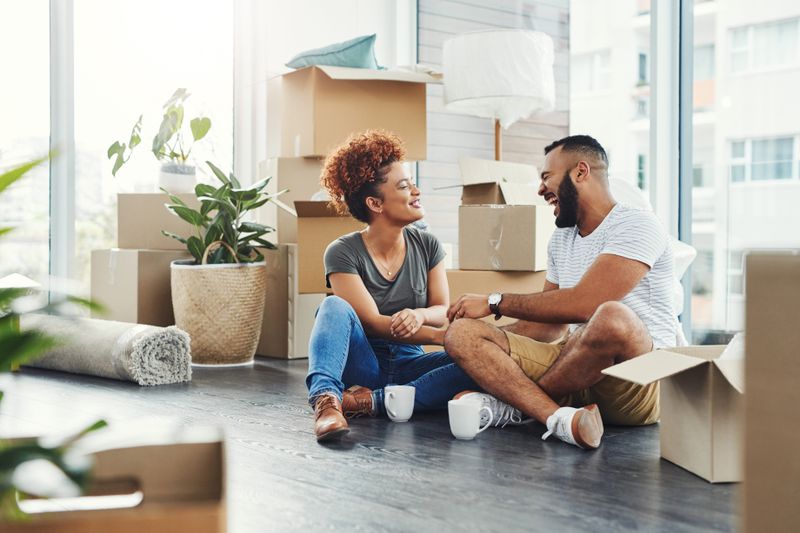 A young couple sits on the floor of a home amid boxes.