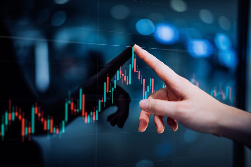 A close-up of a hand pointing to a digital screen displaying a stock market candlestick chart