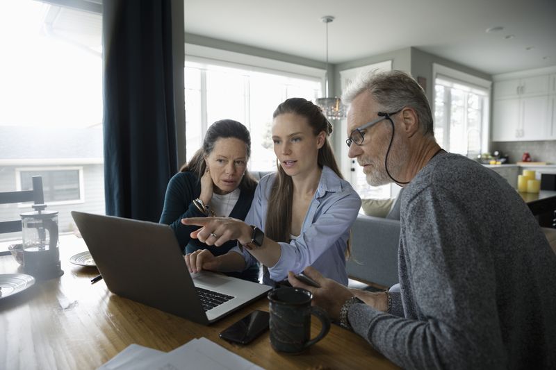 Parents and adult daughter using laptop at dining table.