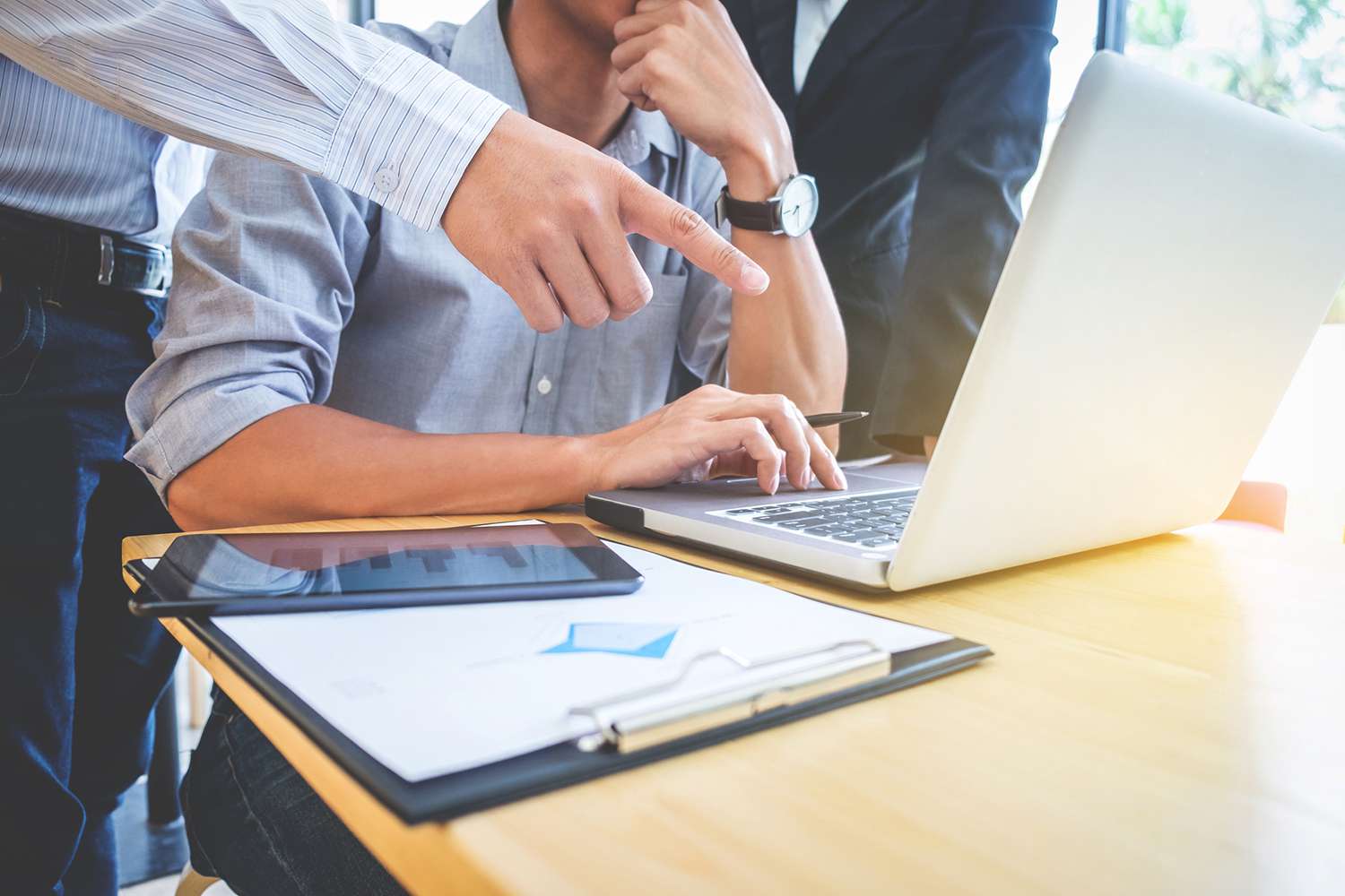 Midsection of Colleagues Discussing Documents at Desk in Office
