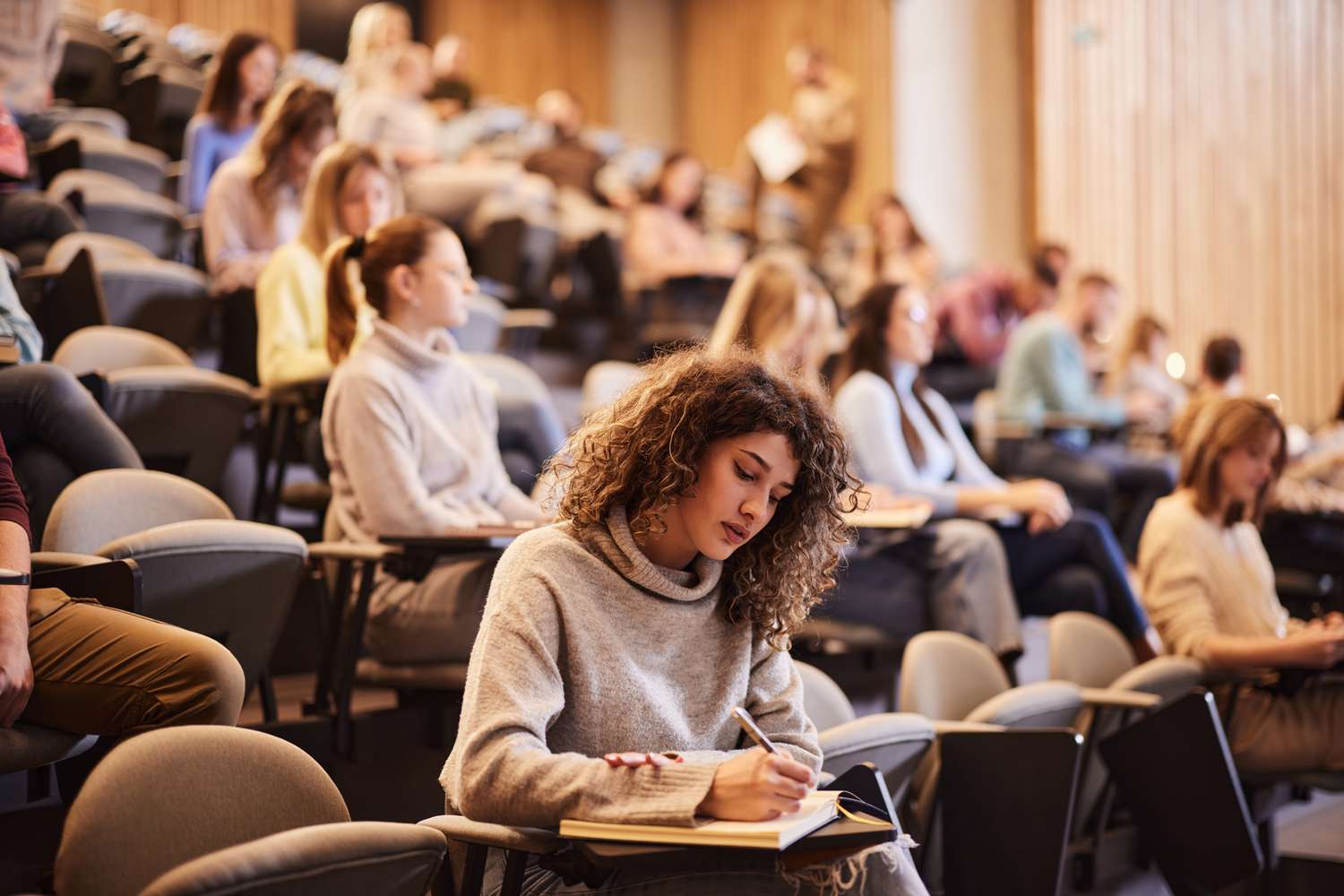 A stock image of a female student in a lecture hall, with other students in the background. 