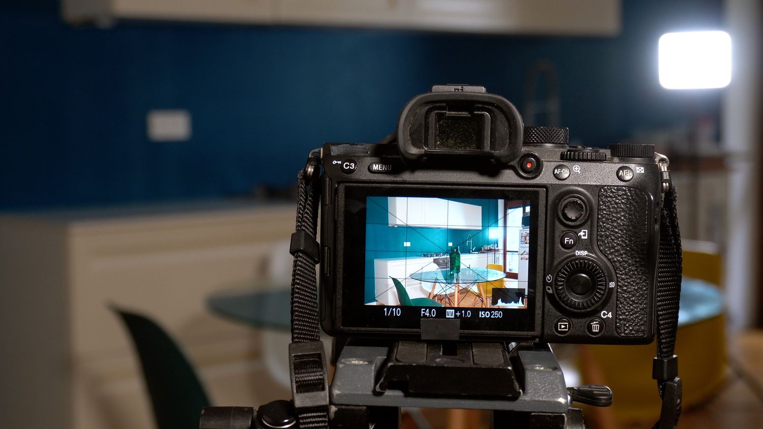 A camera on a tripod capturing a modern kitchen setup seen on its display screen, perspective from behind the camera.