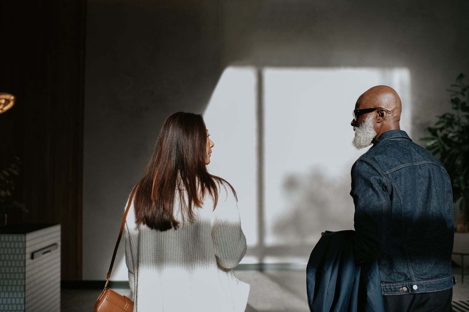 Conceptual image of a woman and man, separated by the shadows on the wall, yet standing next to one another.