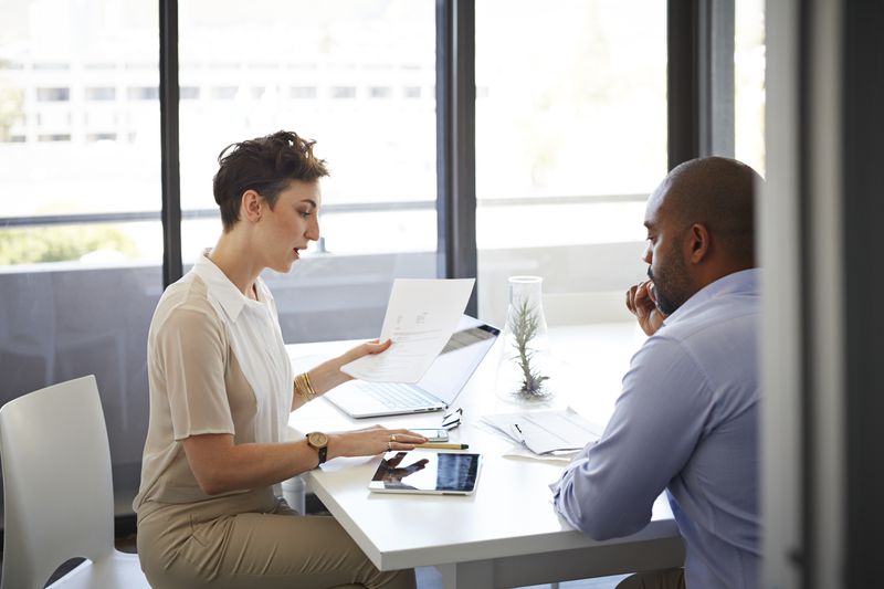 Business colleagues sit at a table in an office and discuss the timing of their upcoming new securities issue and complete SEC Form S-1.