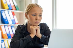 Young woman sitting at a table at the office and looking with concern at a laptop