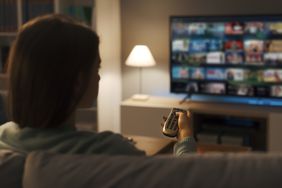 A woman considers what to stream while sitting on the couch. 