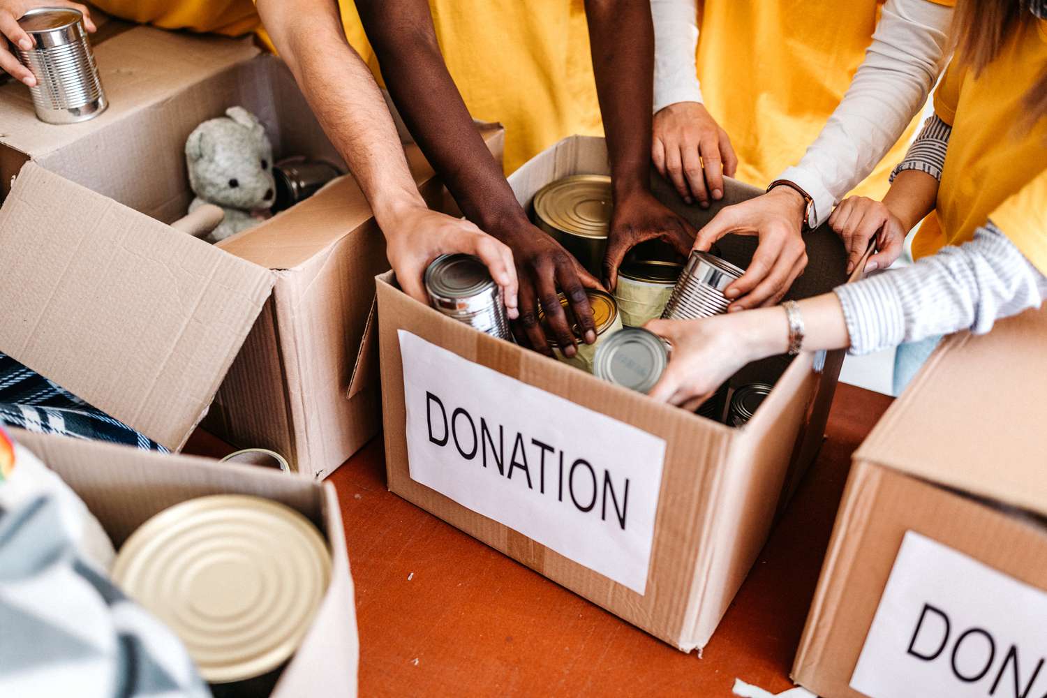 Multiple people reaching hands into a box labeled "donation" 
