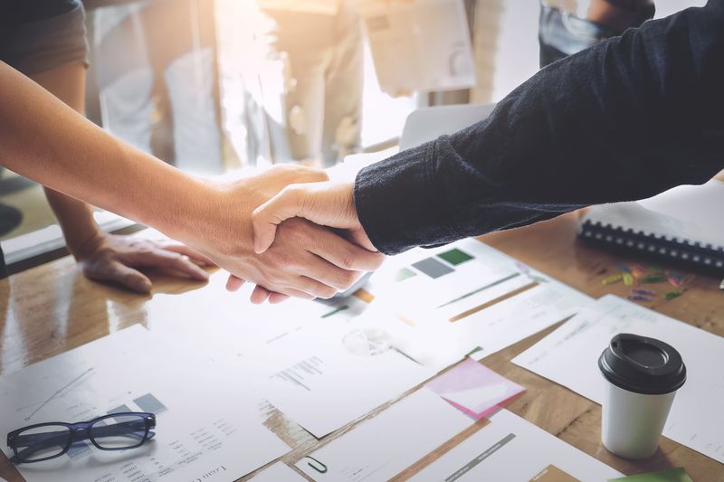 Two people shaking hands over financial documents