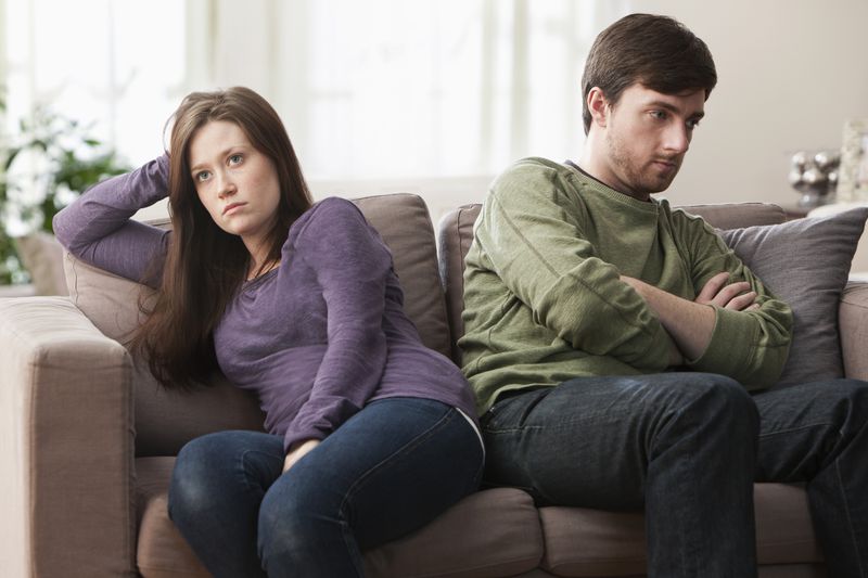 Couple angry at each other sitting on a couch next to each other but facing opposite directions