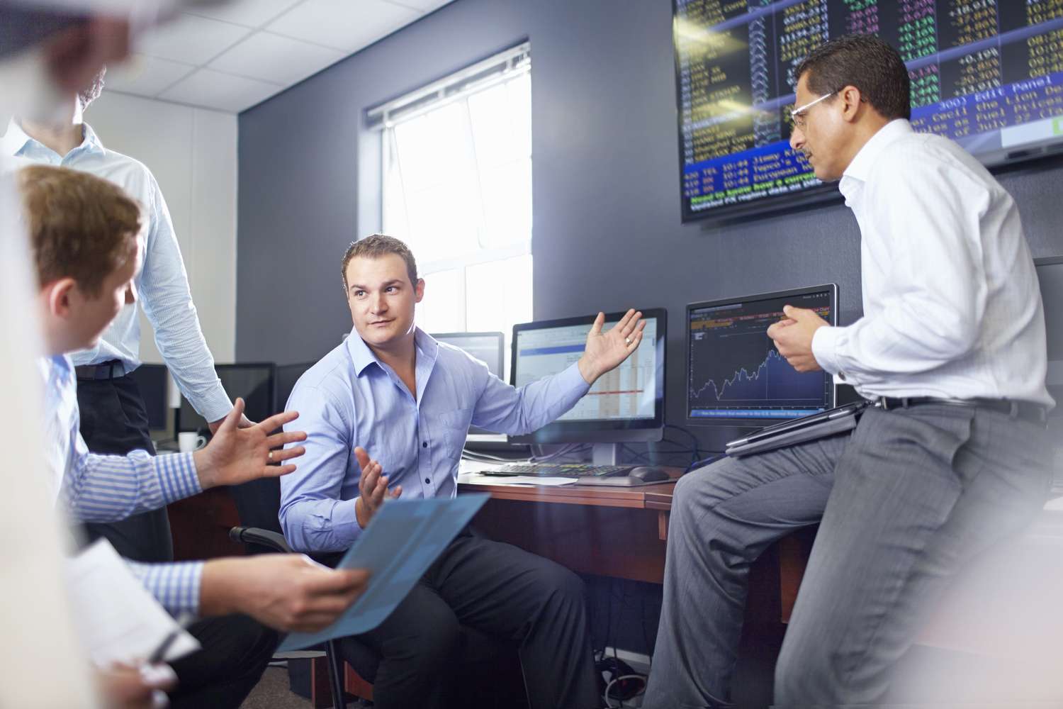 Several colleagues in a stock trading office having a discussion