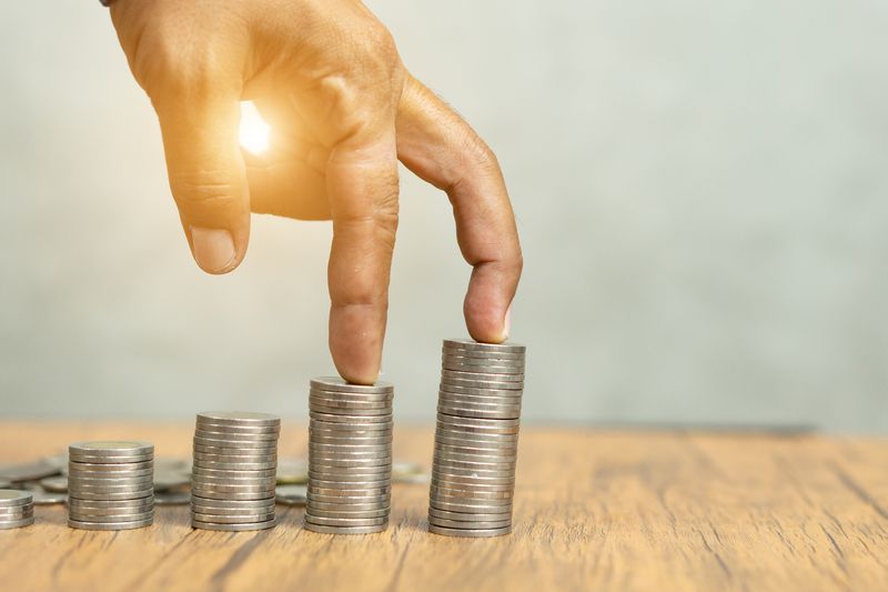 Coins stacked on a wooden table with a hand walking on it.