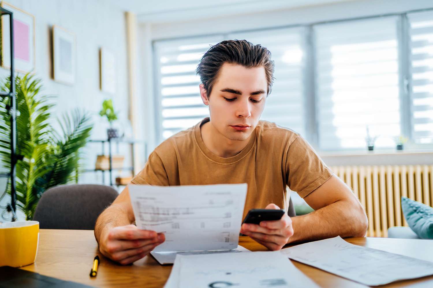 A man sits at a table with a mobile phone and financial documents.