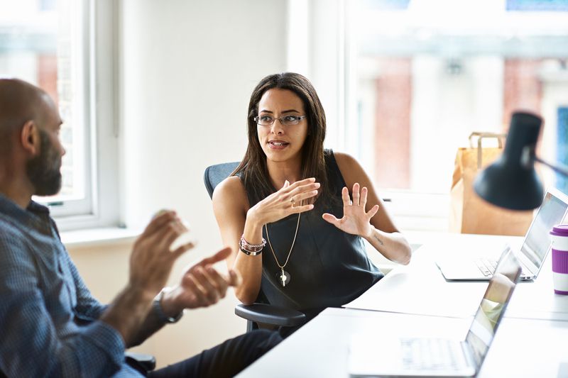 Two people seated at an office table, talking