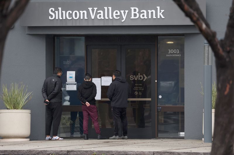 Employees stand outside of the shuttered Silicon Valley Bank headquarters, reading notices posted on the windows. 
