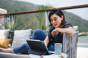 Young Asian woman sitting on the balcony, looking at her finances on a tablet computer.