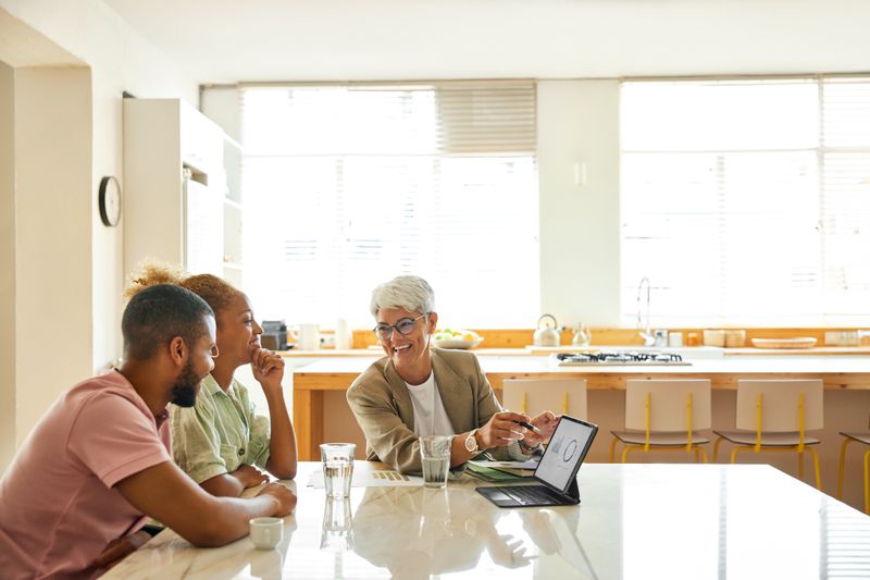 A smiling financial planner works with a young couple in their kitchen.