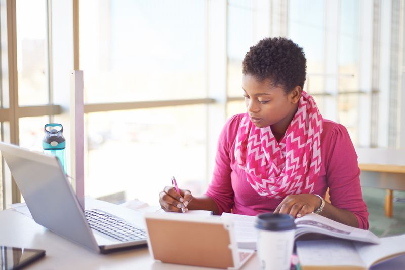 An accountant studies for the Series 53 exam using books and a laptop.