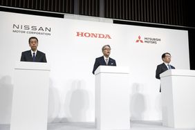 The CEOs of Nissan, Honda, and Mitsubishi are seen standing at white podiums with the logos of their companies on a wall behind them.