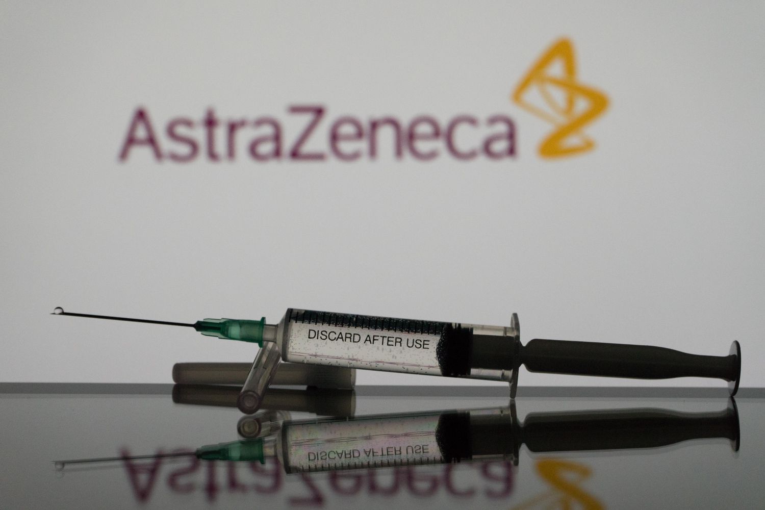 A covid-19 vaccine is seen with the AstraZeneca logo in the background