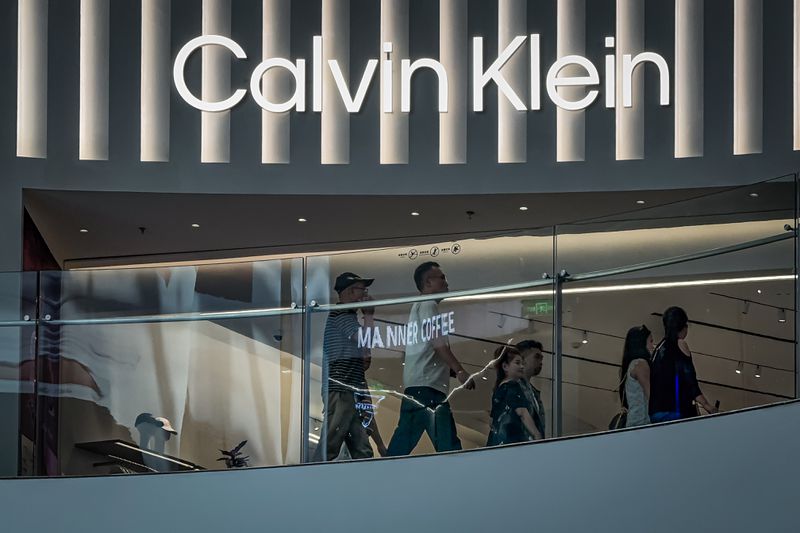 Shoppers walk past a Calvin Klein store beneath illuminated signage inside a modern shopping mall on May 20, 2025 in Chongqing, China