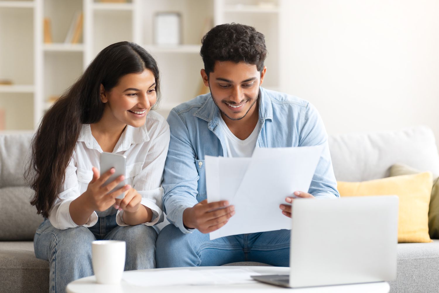 Young couple sitting on their sofa and looking at mortgage documents and rates on their laptop