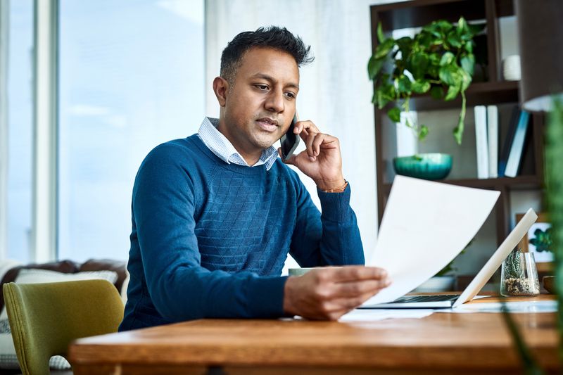 A man talks on the phone while holding documents to ask about the max amount for personal loan. 