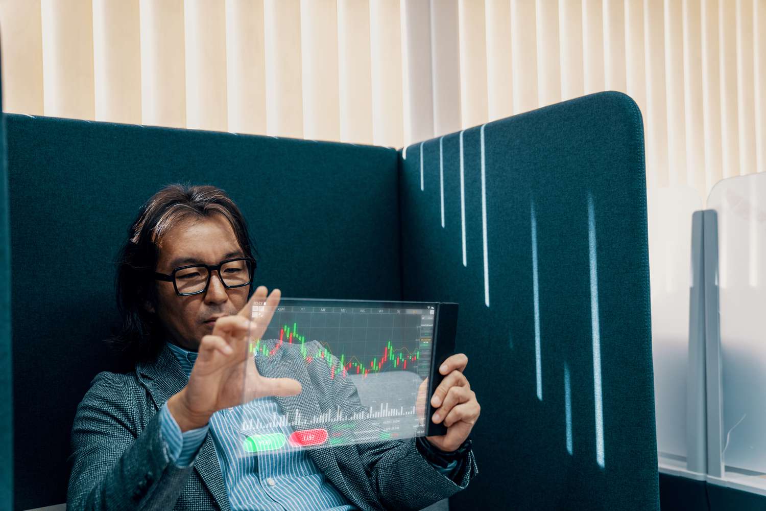 A man in a chair examines market data using a futuristic tablet-style device. 
