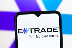 The E*Trade logo is seen on a phone screen, with a larger version of the logo in the background.