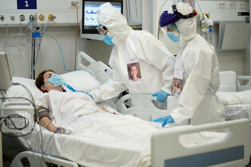 Masked woman on ventilator, with two medical workers in full pandemic PPE