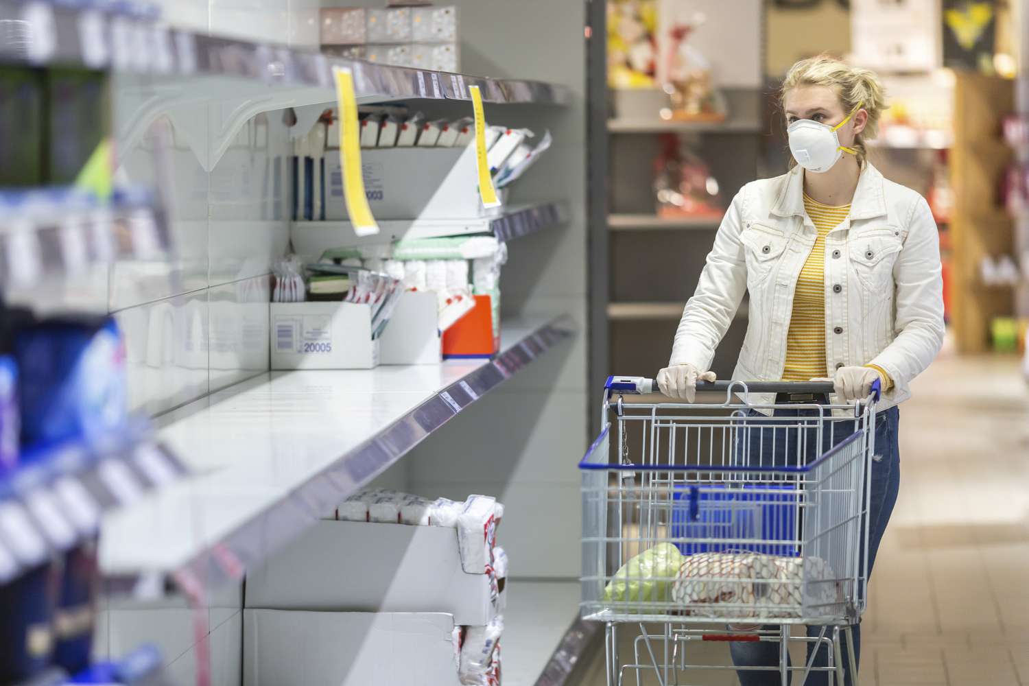 Shopper wearing mask looking at empty shelf in a store due to supply shock caused by COVID-19.