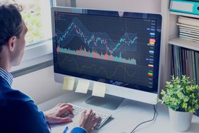 A man types on a keyboard in front of a computer screen displaying stock charts.
