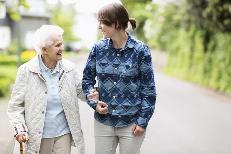 Young woman helping elderly woman walk down street.