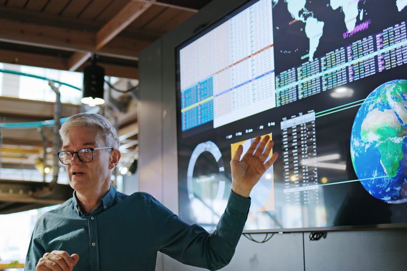 Man standing before a screen showing a globe