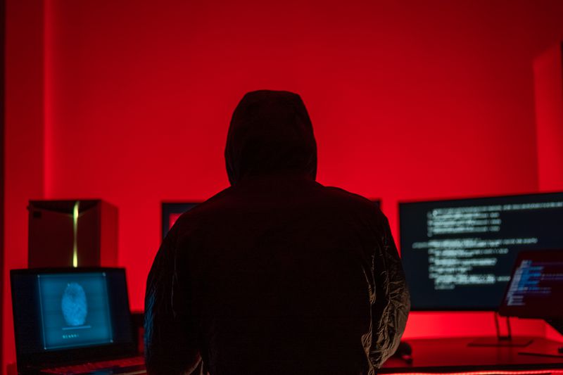 A representation of a hooded hacker working in a red-lit computer room.