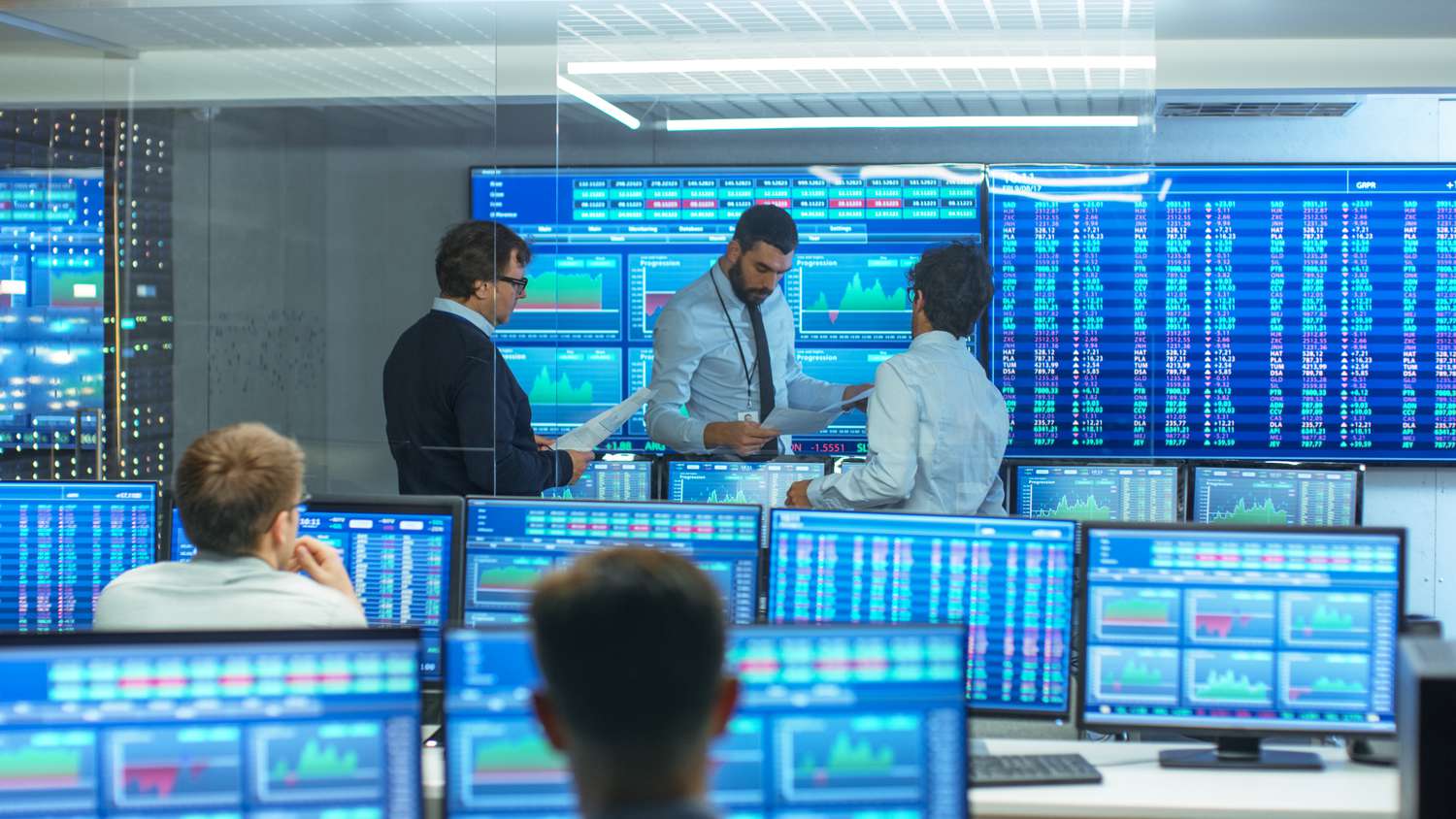 Brokers, traders, and analysts work in a trading room full of computers and monitors as they handle customer orders and monitor the stock exchange.