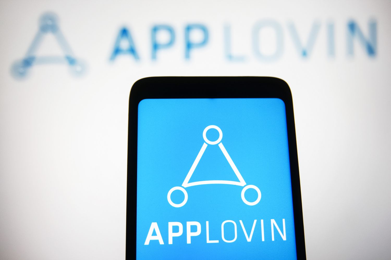 The blue Applovin logo is seen on a phone screen ahead of a white background that also says Applovin