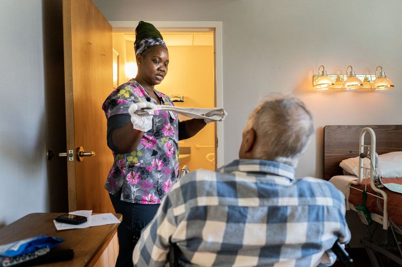 Caregiver assisting a seated elderly individual in a bedroom setting