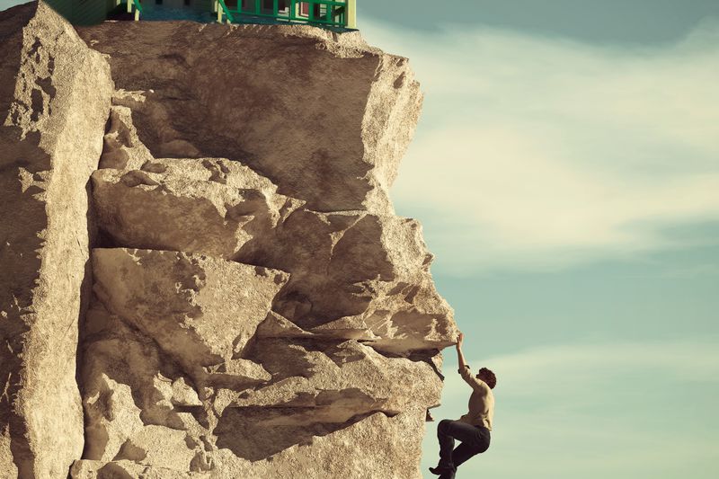 A man climbing a rock face toward a house