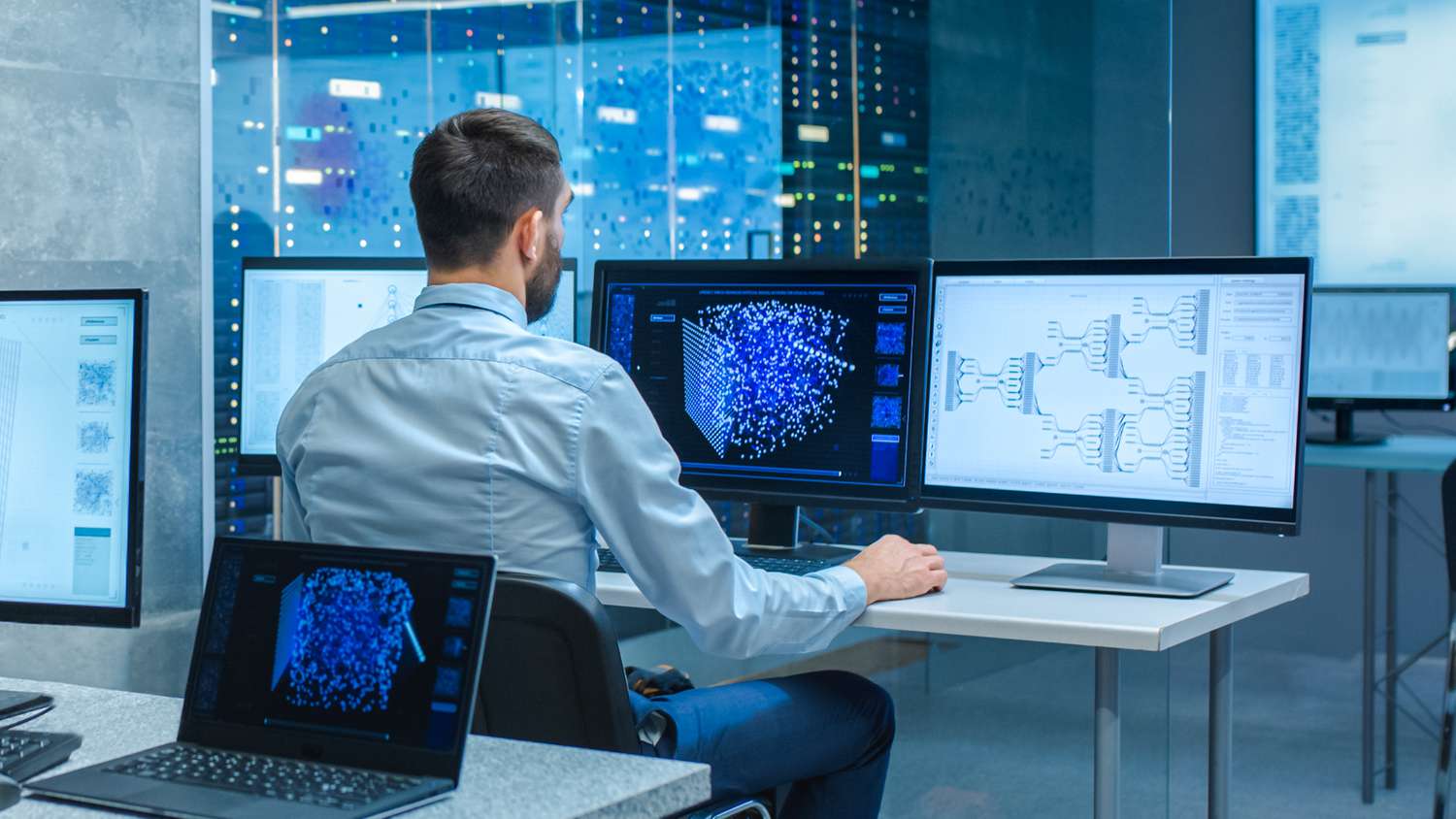 Computer engineer at workstation in office that is full of displays showing 3D representations of neural networks