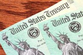 Two US Treasury checks of the type used to pay tax refunds as well as Medicare, Social Security and welfare benefits are partially visible on a wood desk background. Checks show the Treasury seal and image of the Statue of Liberty. 