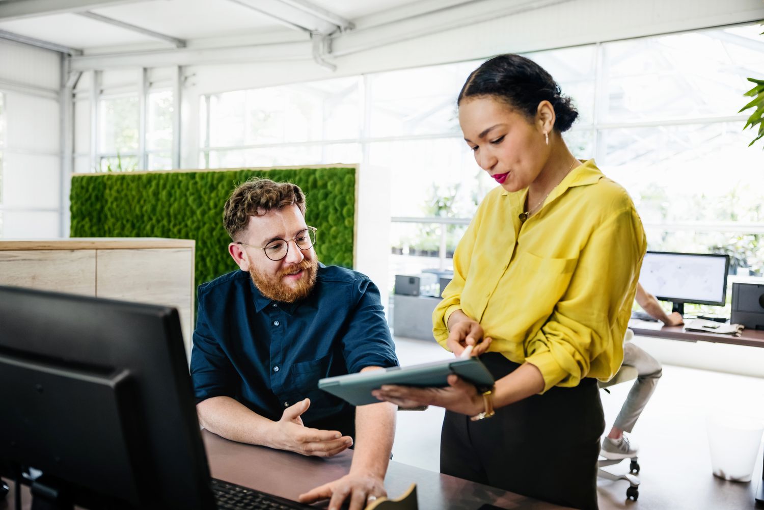 An office manager showing some documents on a digital tablet to a colleague in a bright, modern office.