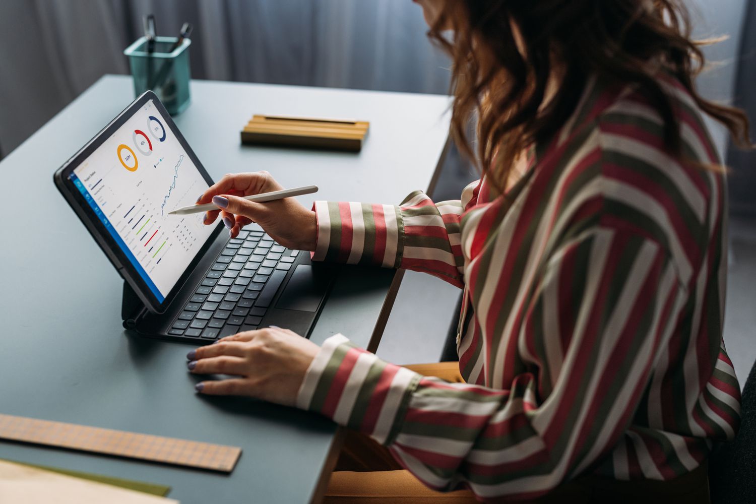 Focused young female analyzing financial statistics on digital tablet, working from a modern home office setup.
