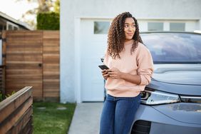 A woman leans on a car. 