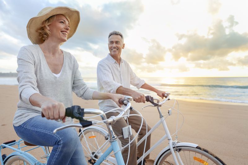 Mature couple cycling on the beach at sunset or sunrise in Australia.